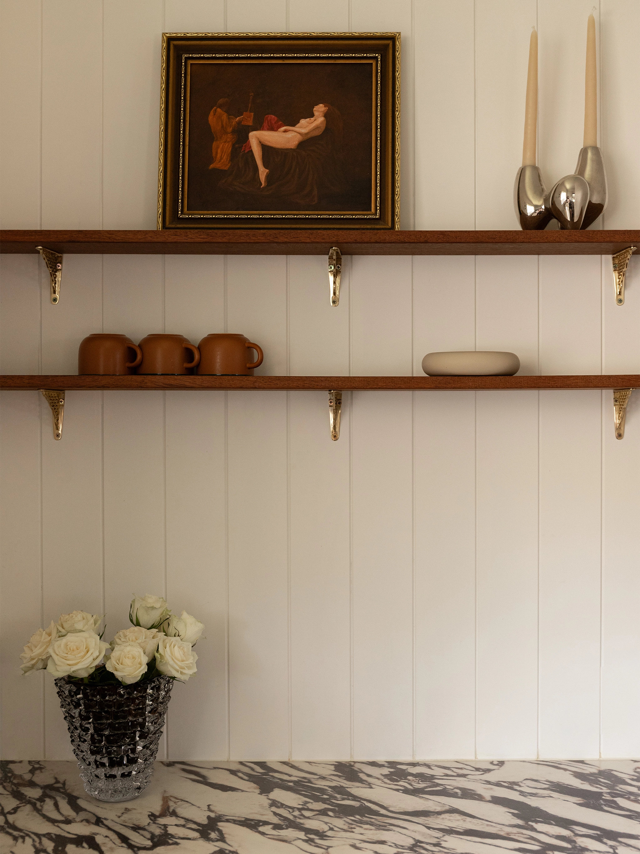 Shelves with decorative items against a white panelled wall, brown glass vase, rostrato texture with white roses.