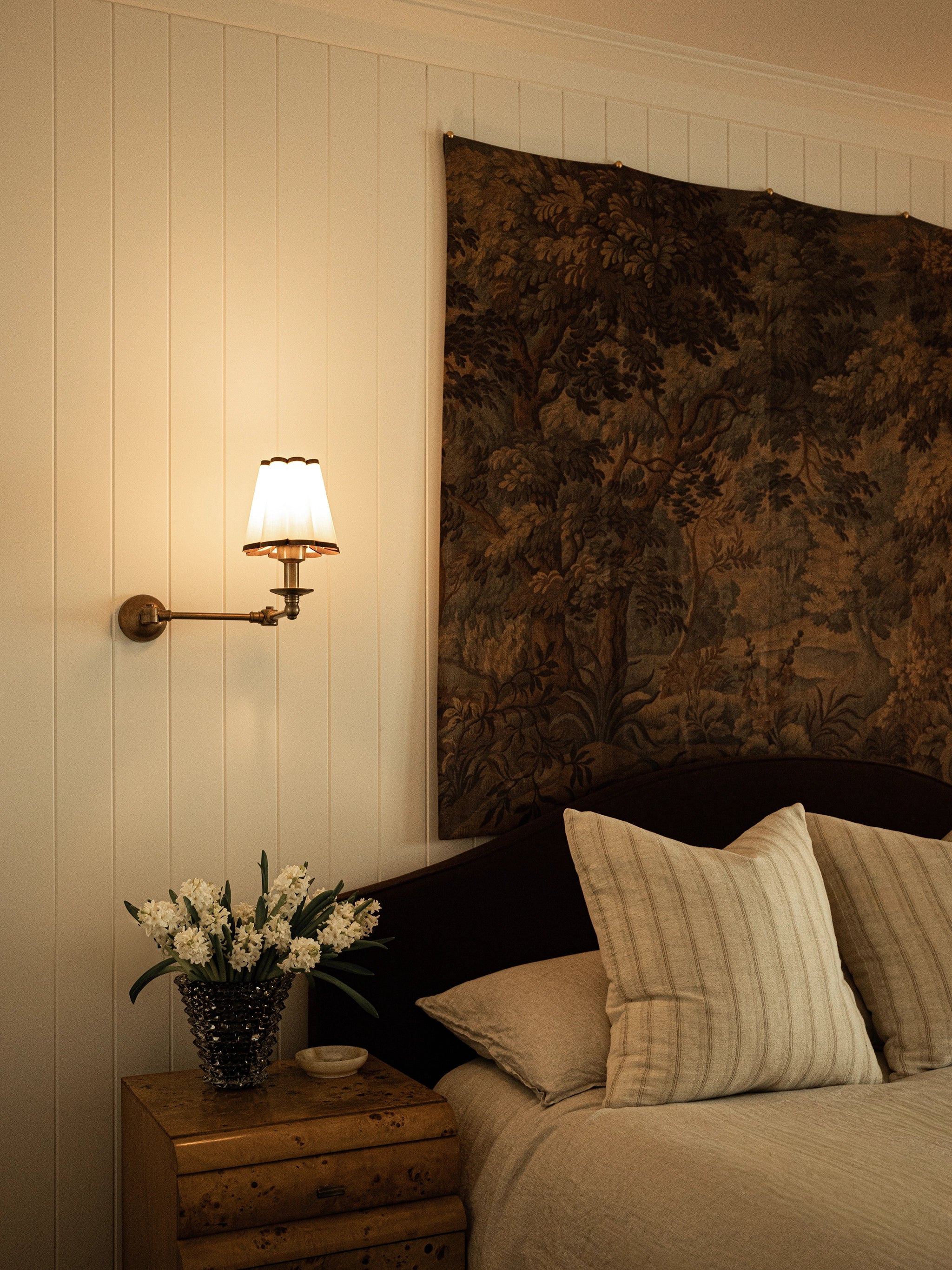 Bedroom with floral arrangement on nightstand and decorative tapestry above headboard.