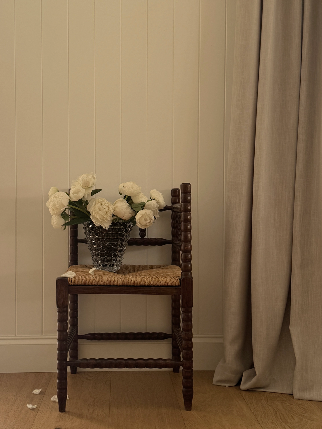 Brown Node glass vase sitting on a vintage bobbin corner chair with white wilting peonies